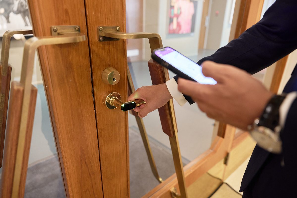 A hand on a brass door handle with a Bitwards reader in it, showing green, while the other hand holds the phone that opened it