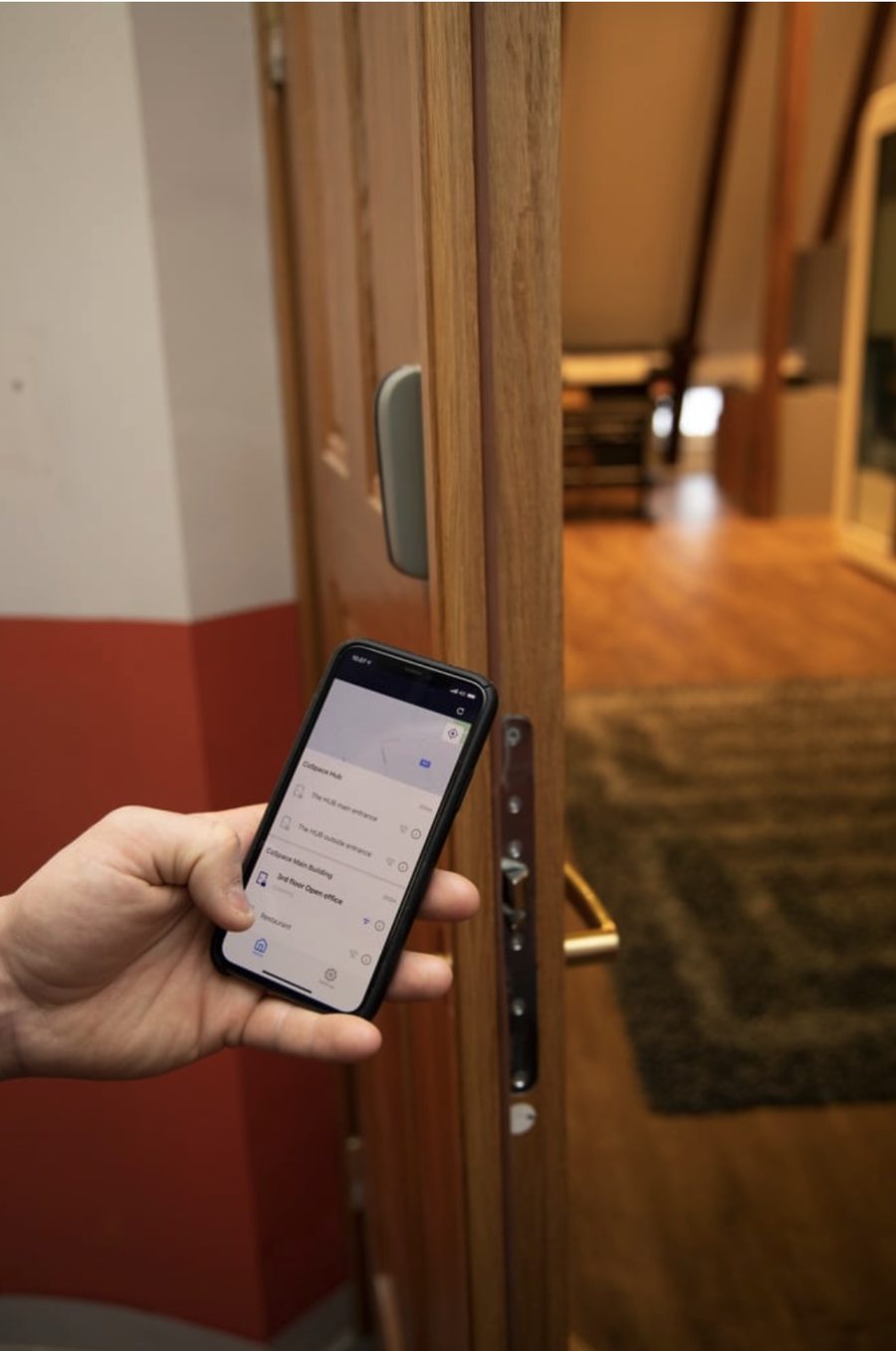A hand holding a phone showing the CoSpace doors in the Bitwards app, beside an open office door