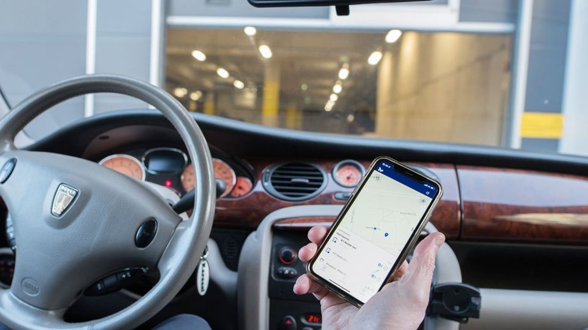 A driver holding a phone showing the Bitwards app, the garage entrance visible through the windscreen