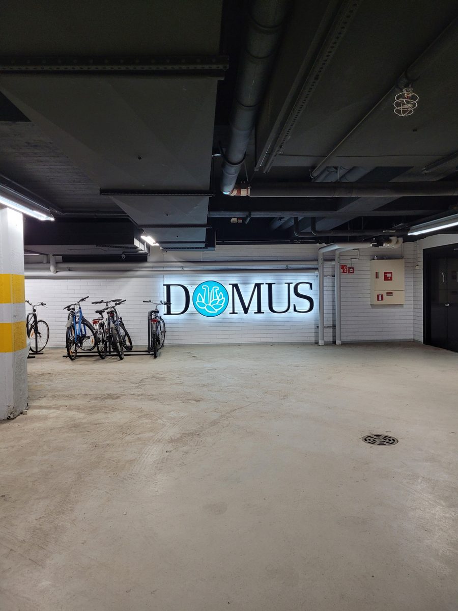 The Domus car park, bicycles racked against a white brick wall under the lit Domus sign