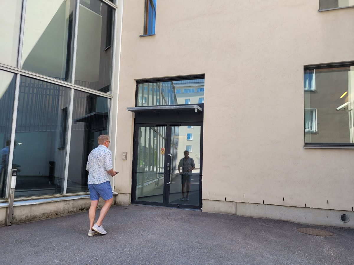 A man walking to a side entrance with his phone in his hand, past the old keypad on the wall